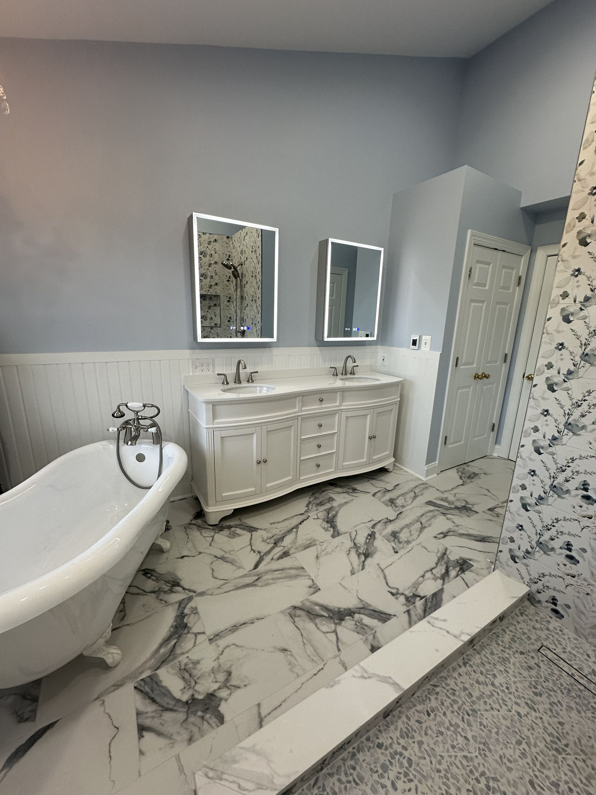 Modern white bathroom with freestanding tub, marble tile floor, vanity, and mirrored cabinets.
