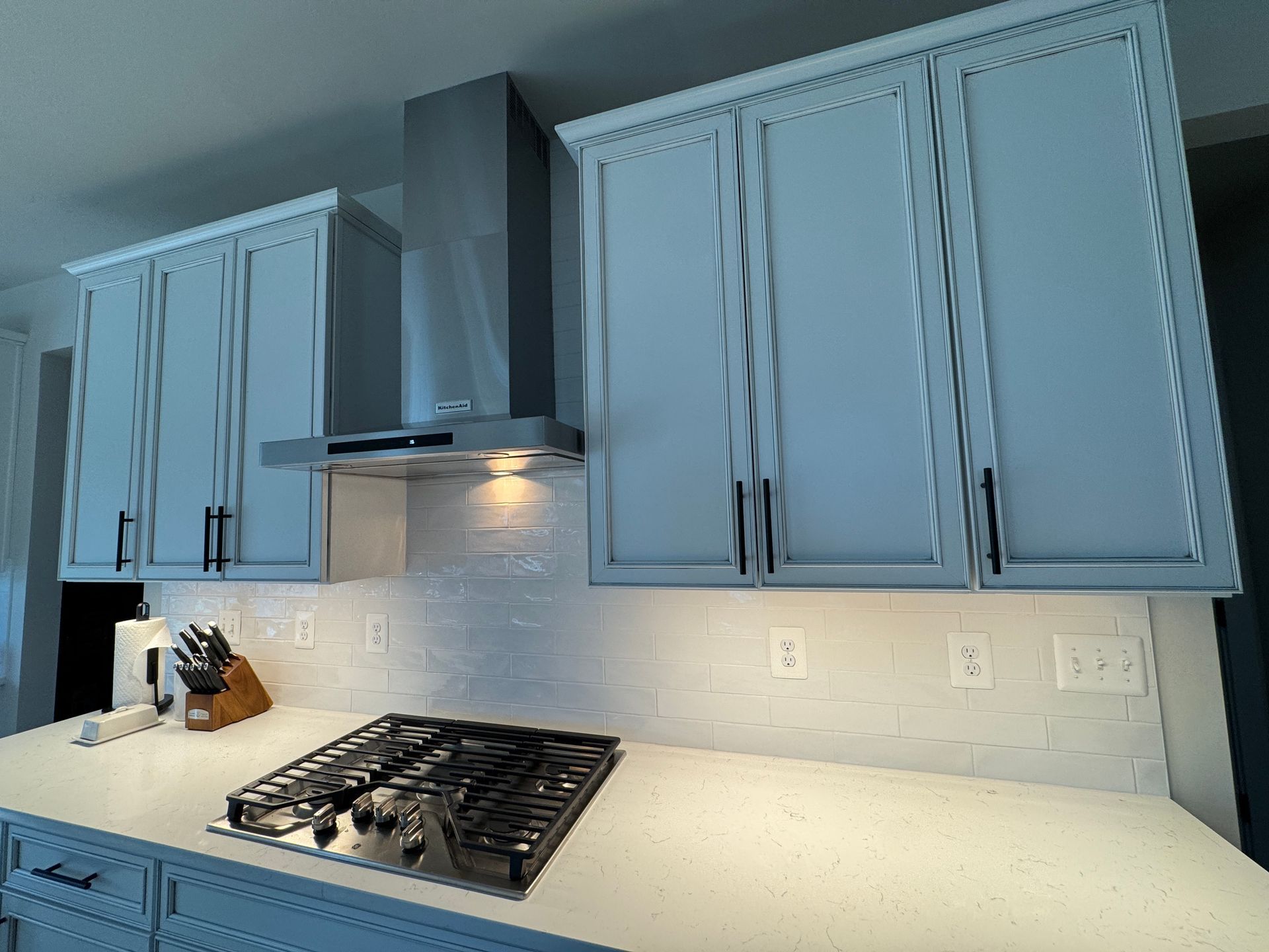 Modern kitchen with light blue cabinets, stainless hood, gas stove, and white tile backsplash