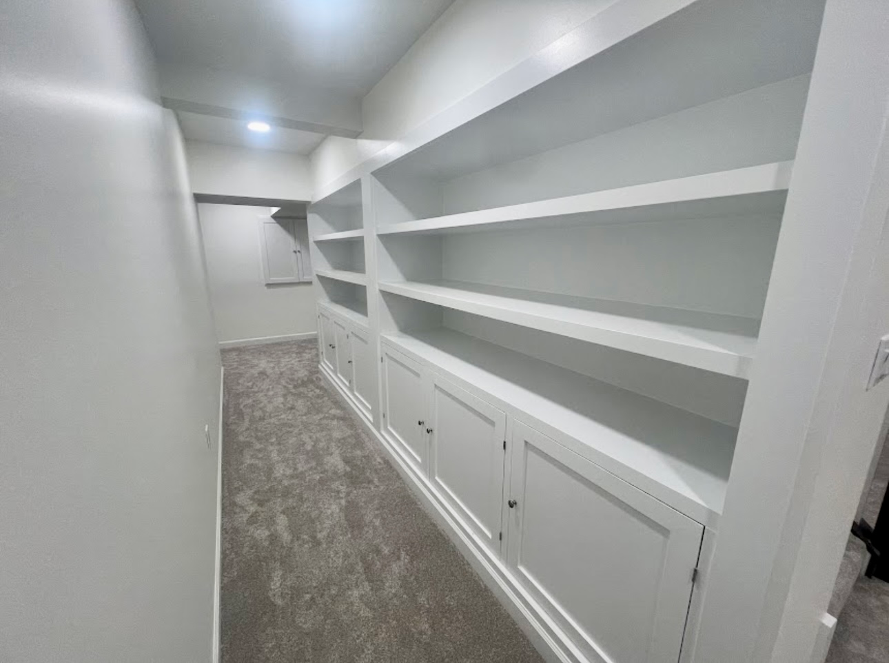 White built-in shelving and cabinets in a narrow carpeted room with recessed ceiling lights