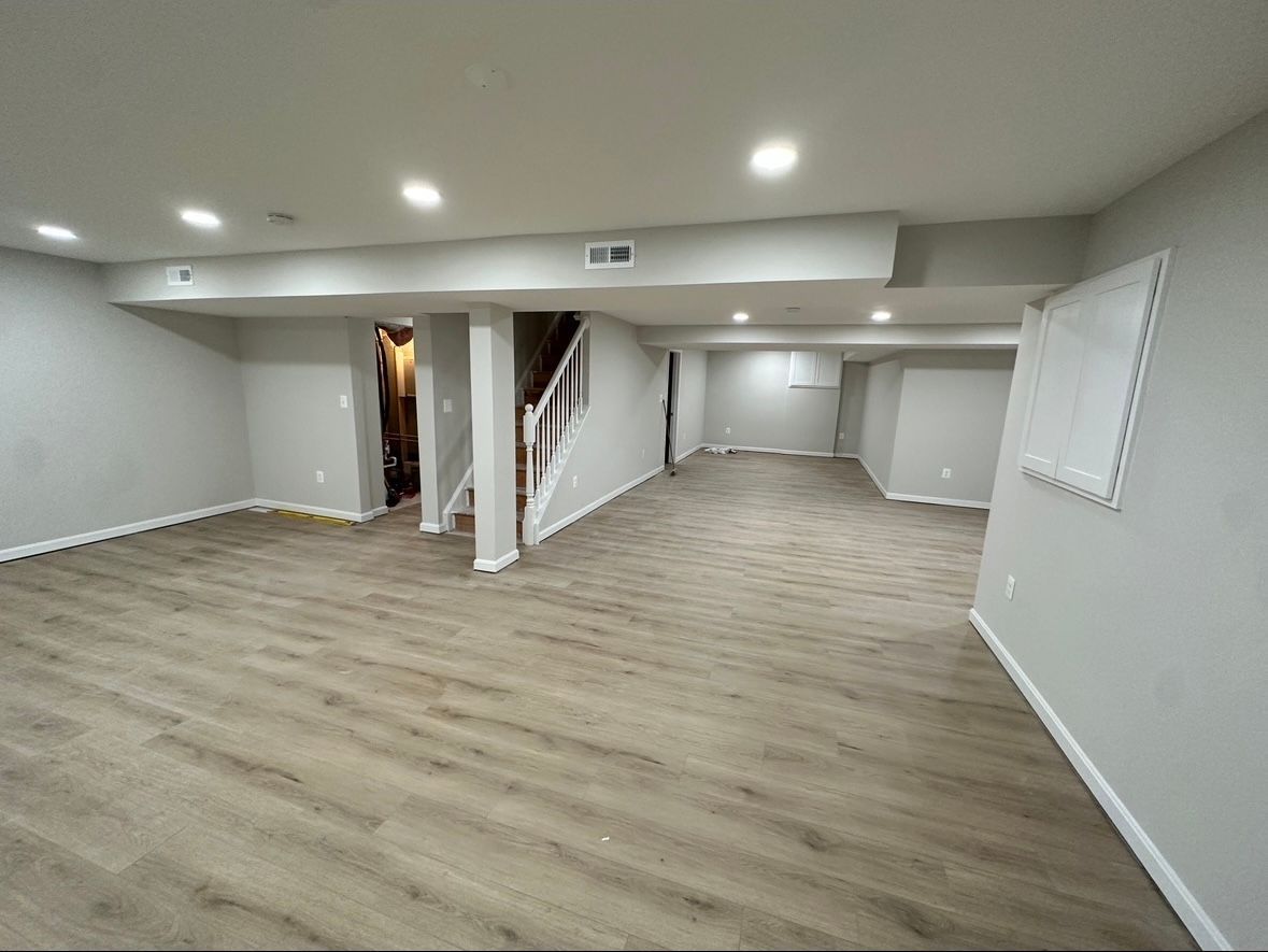 Empty finished basement with gray walls, light wood floors, recessed lights, and stairs to the left.