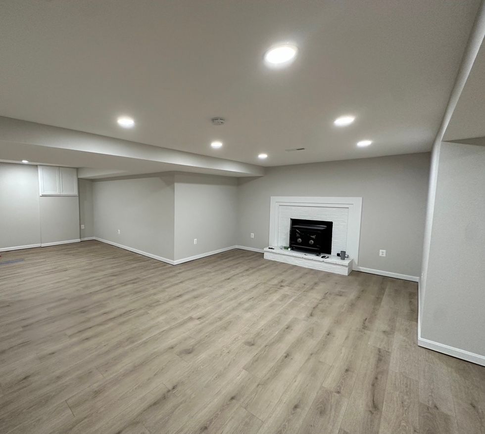 Empty modern living room with light wood floors, recessed lights, and a white fireplace mantel