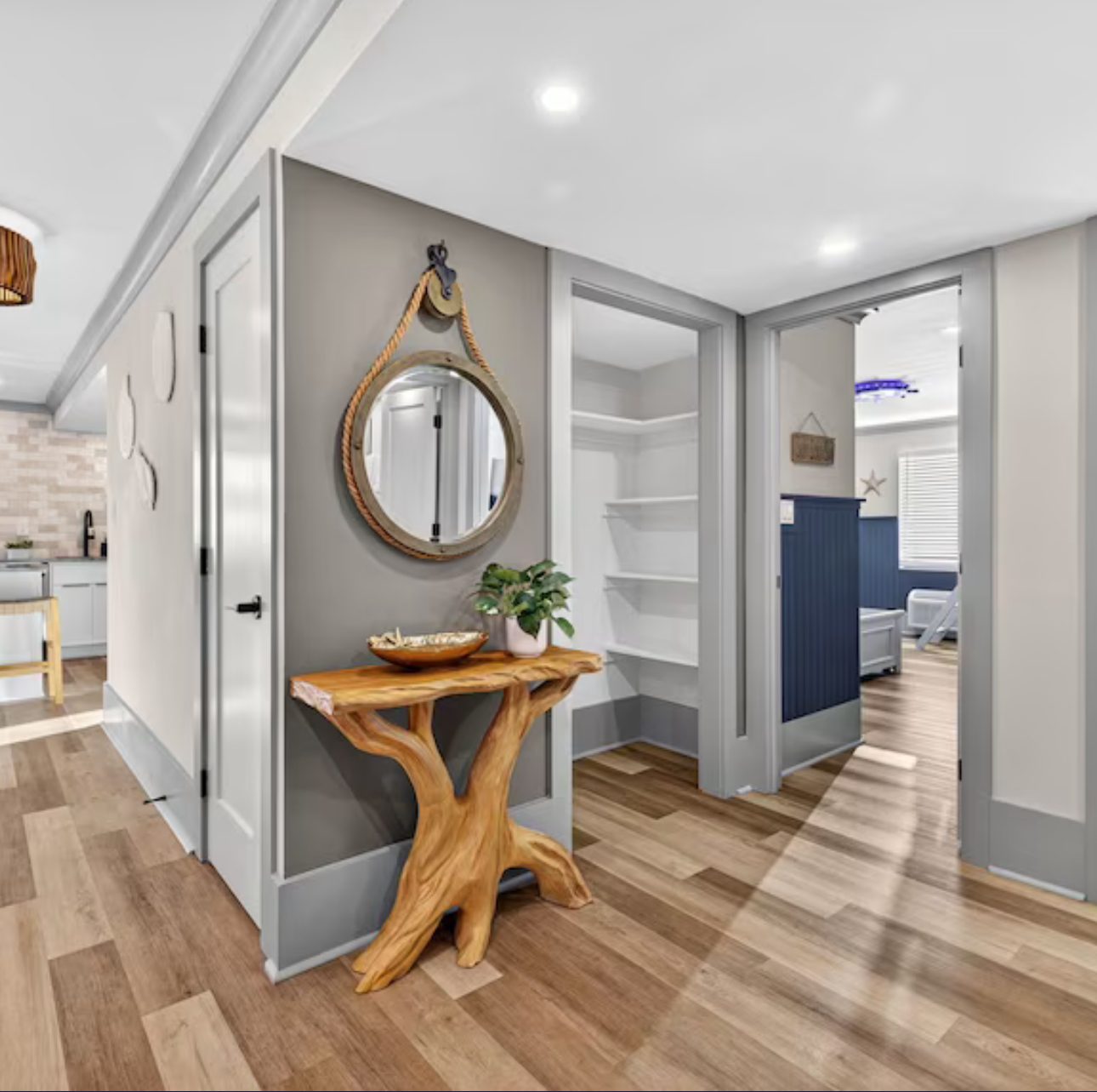 Bright hallway with gray walls, wood floors, round mirror, and a rustic console table with plant and bowl.