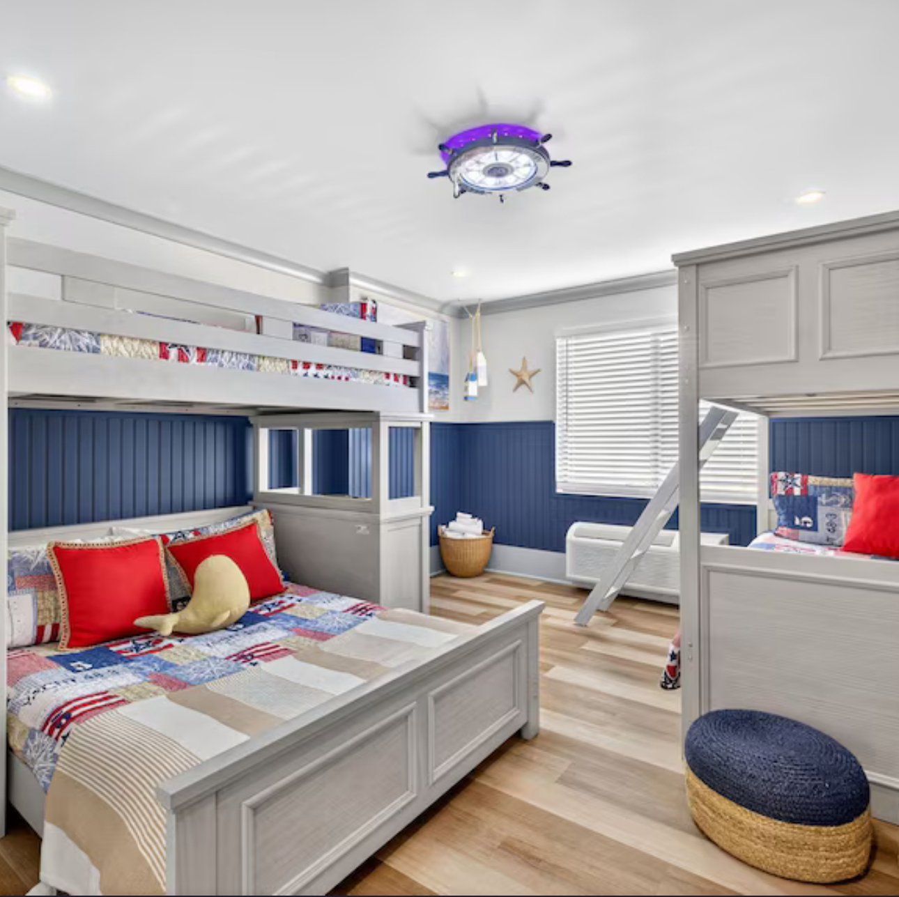 Bright child’s bedroom with bunk beds, navy walls, and light wood floors, featuring red and blue bedding