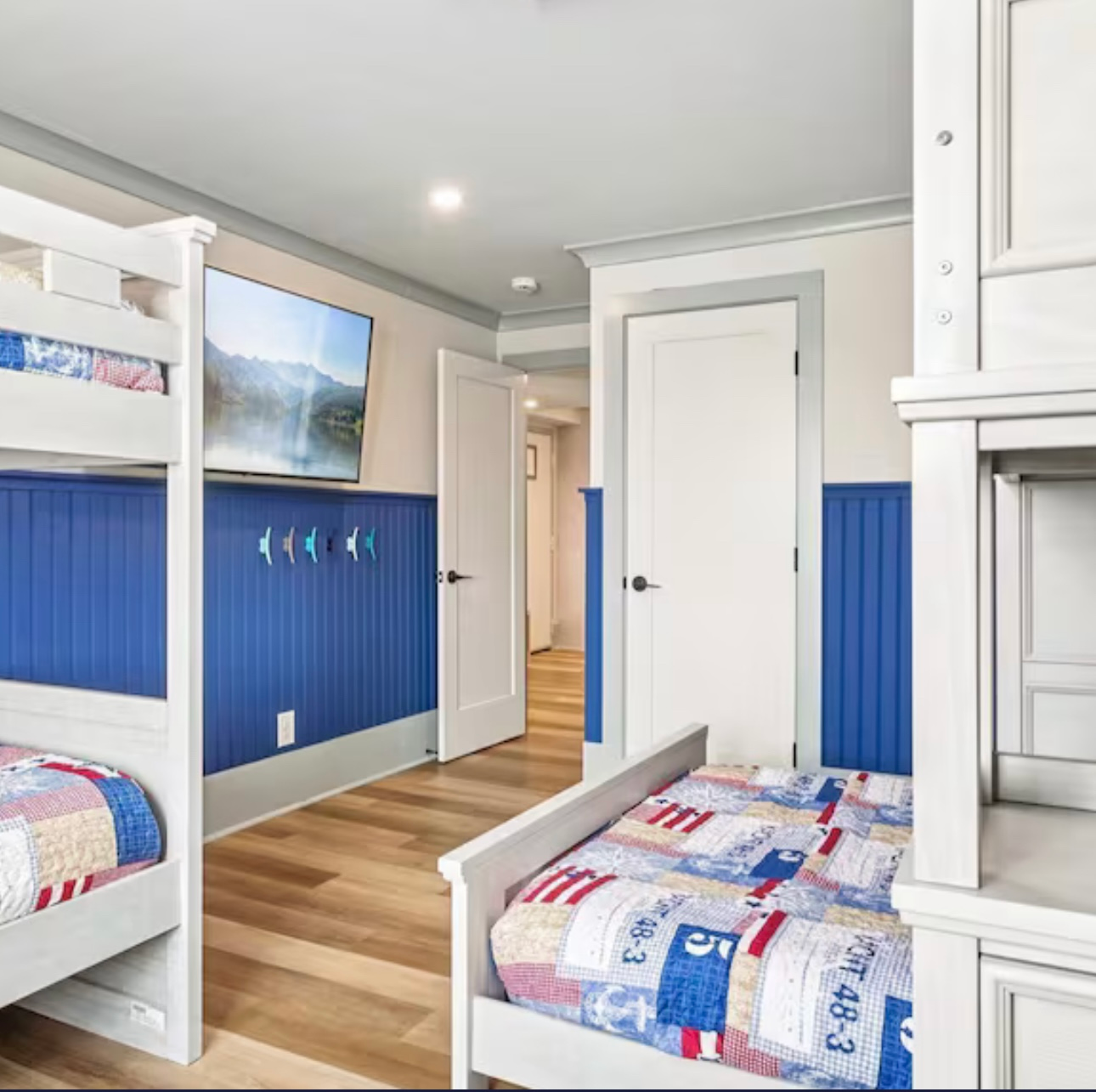 Navy and white bunk room with twin beds, wood floor, wall art, and doorway to a hallway