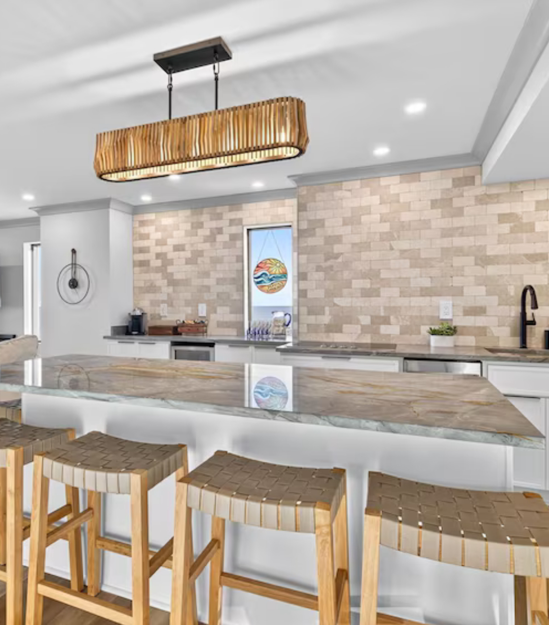 Modern kitchen with white island, marble counters, wicker stools, and beige tile backsplash