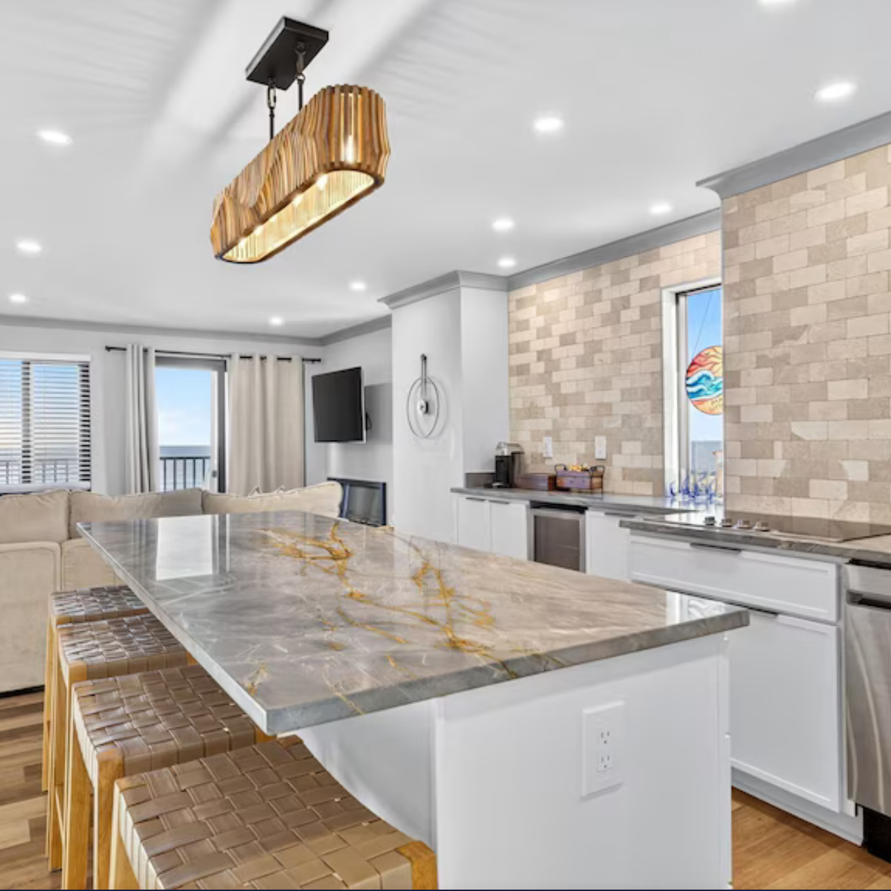 Bright modern kitchen with marble island, woven stools, white cabinets, and gold pendant light