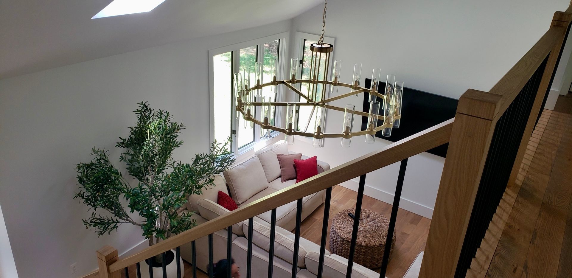 Staircase overlooking a bright living room with a chandelier, sofa, and potted tree.