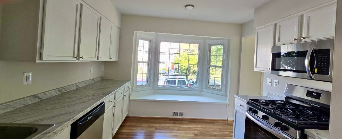 Bright white kitchen with granite counters, stainless appliances, and a large window over the sink.