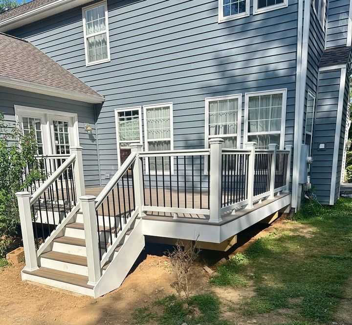 Small white-railed wooden deck and stairs attached to a blue house in a sunny yard