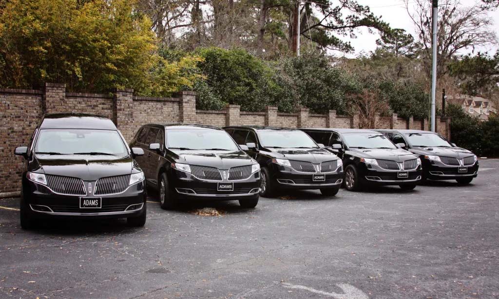 A row of black cars are parked in a parking lot.