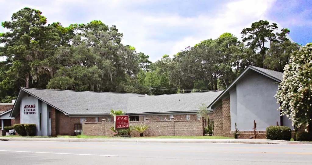 A brick building with a gray roof is surrounded by trees