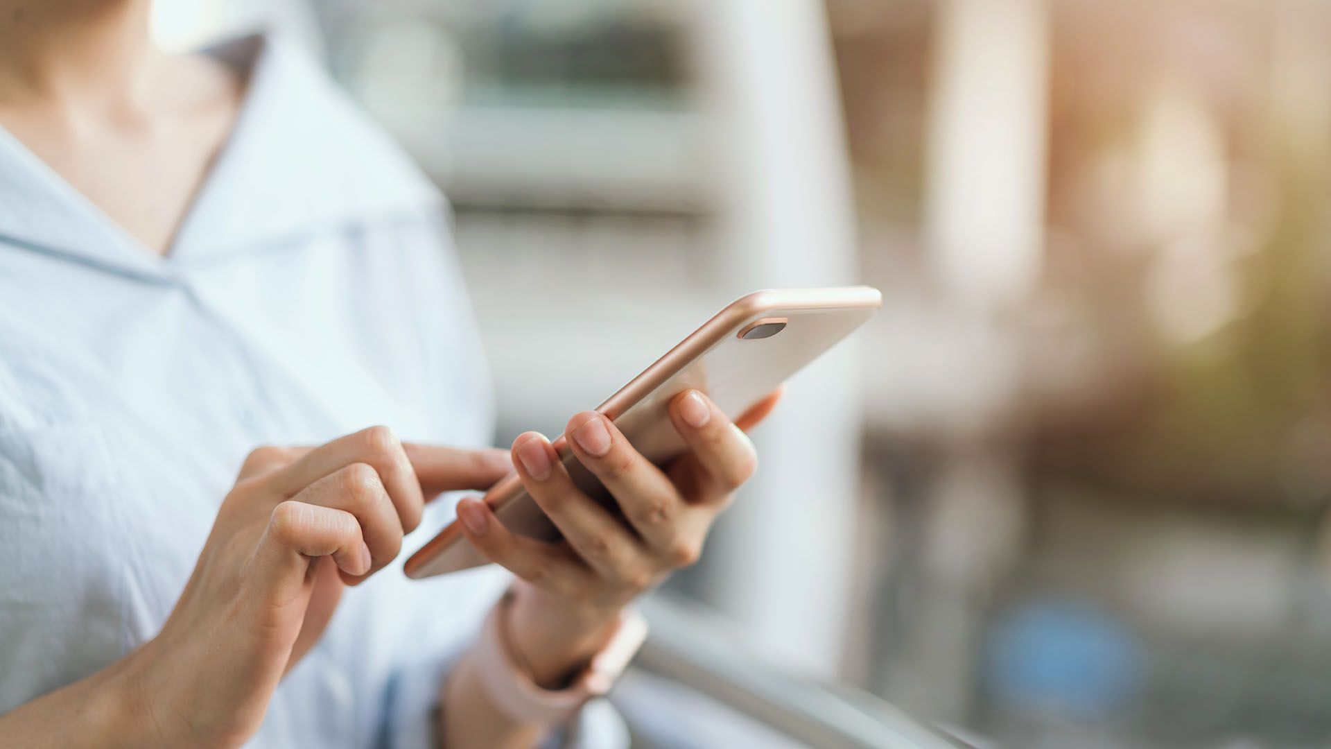 A woman is using a smart phone while standing next to a window.