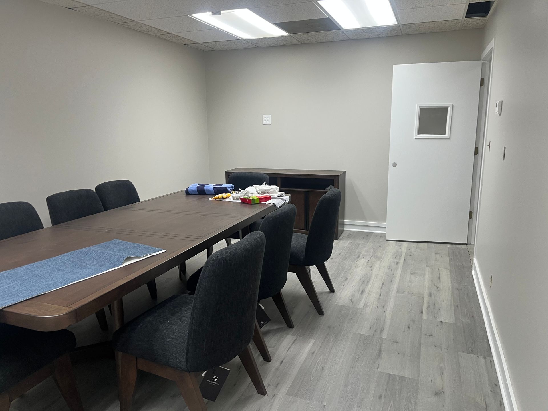 Small conference room with long table, black chairs, and a white door at the back.