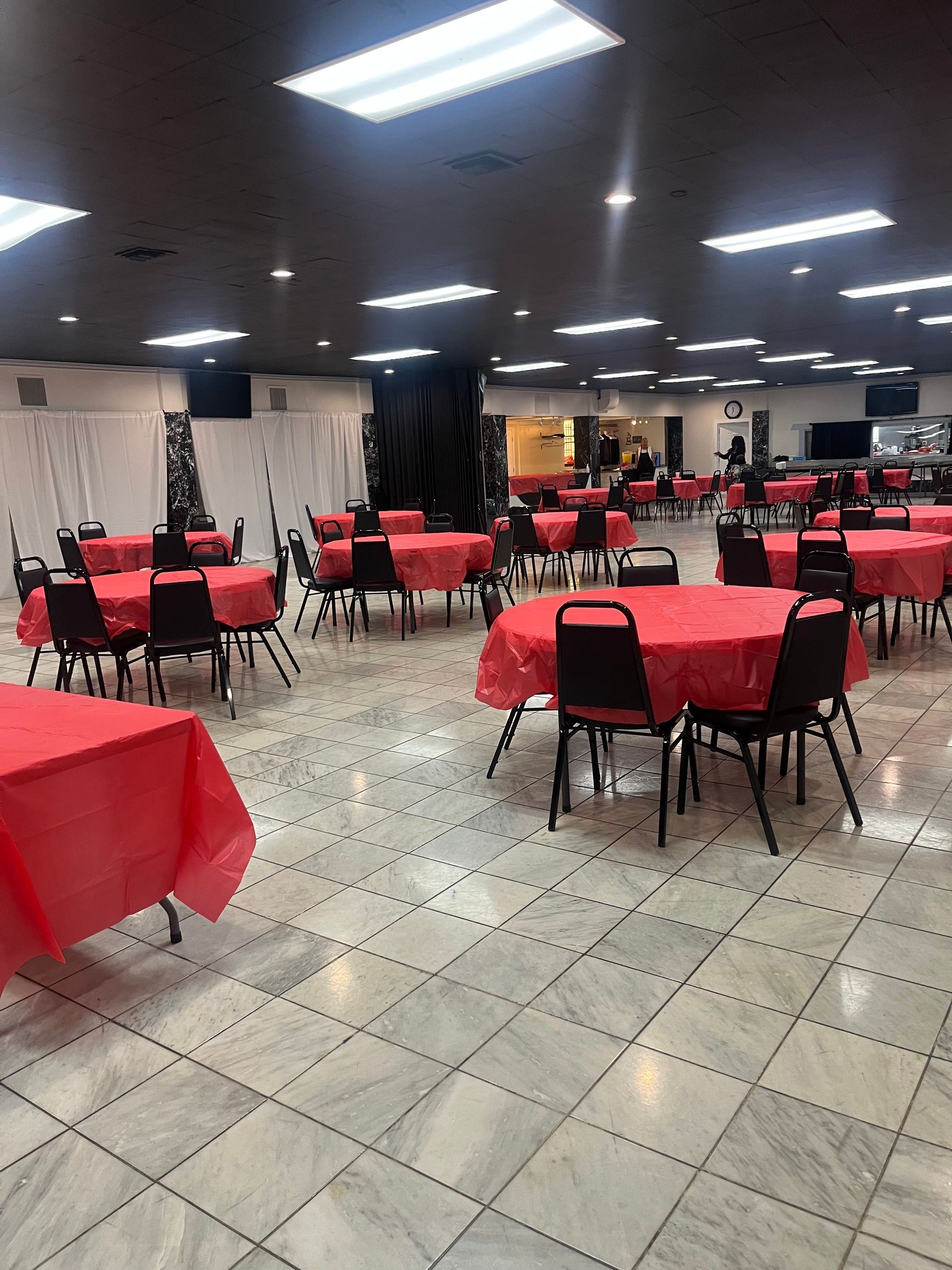 Empty banquet hall with red tablecloths and black chairs under bright ceiling lights