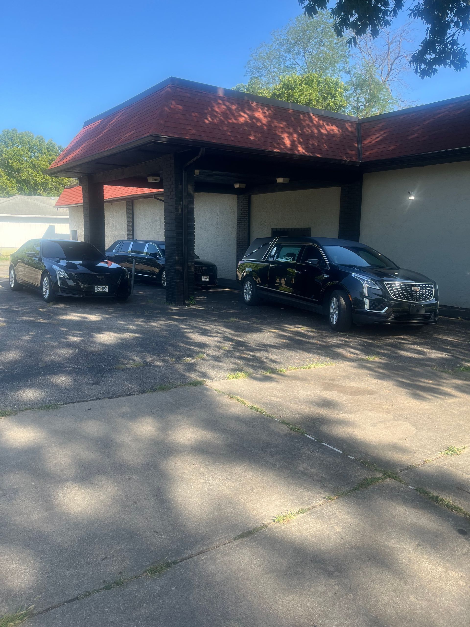 Three black cars parked under a red-roofed carport beside a light-colored building.