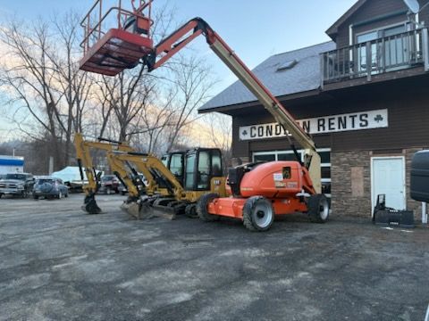 An orange aerial lift and a yellow excavator parked in front of a rental business.