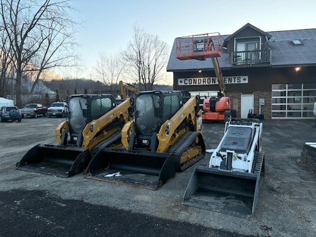 Three yellow and white construction vehicles with buckets parked in front of a building.