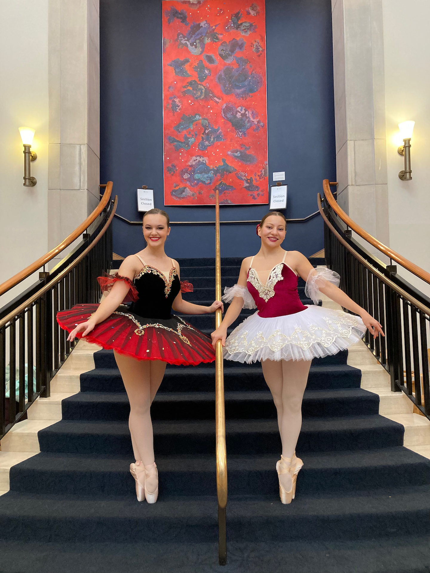 Two ballet dancers pose on a grand staircase in red and white tutus.