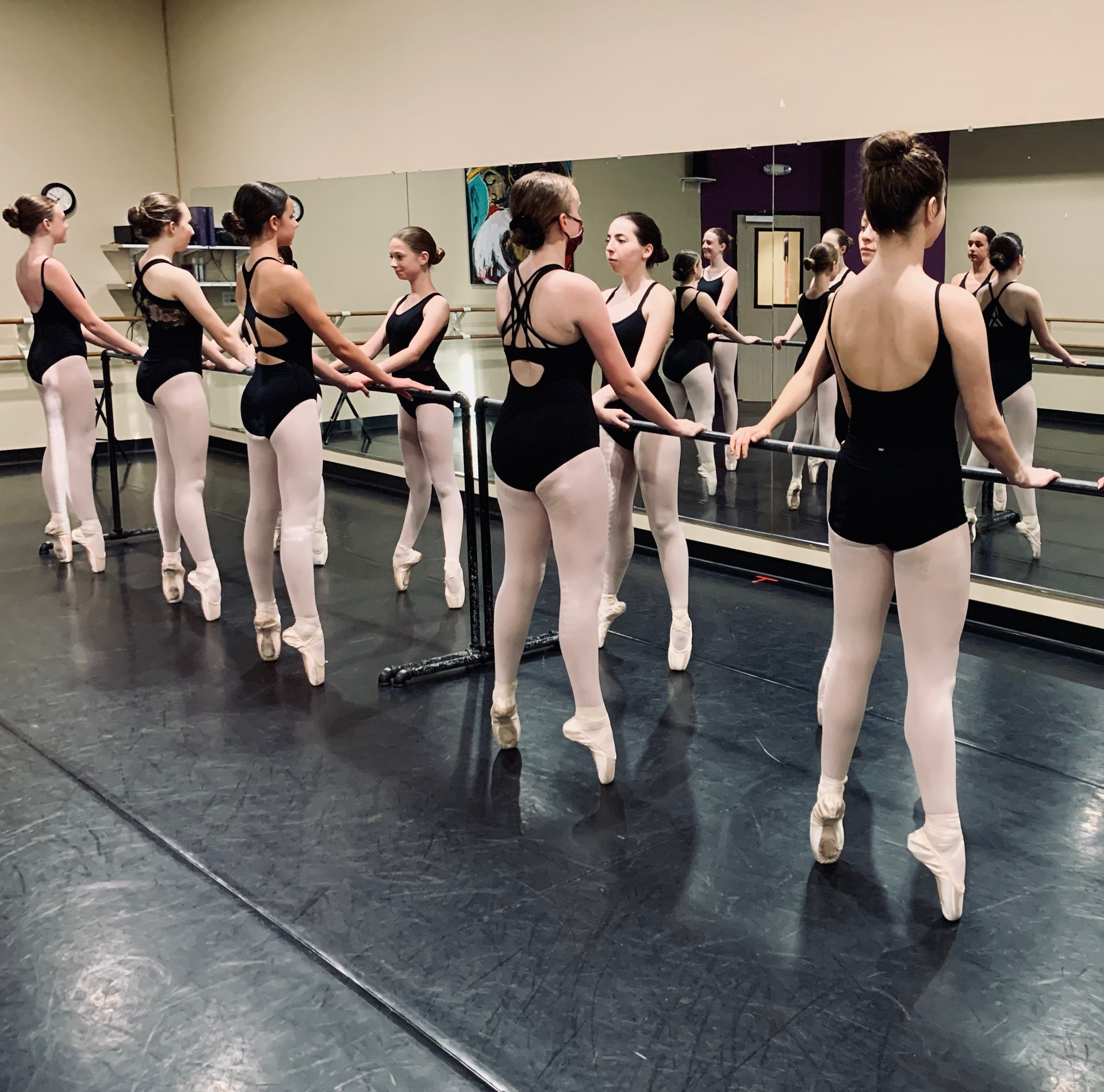 Ballet class at the barre with dancers in black leotards and pink tights in a mirrored studio