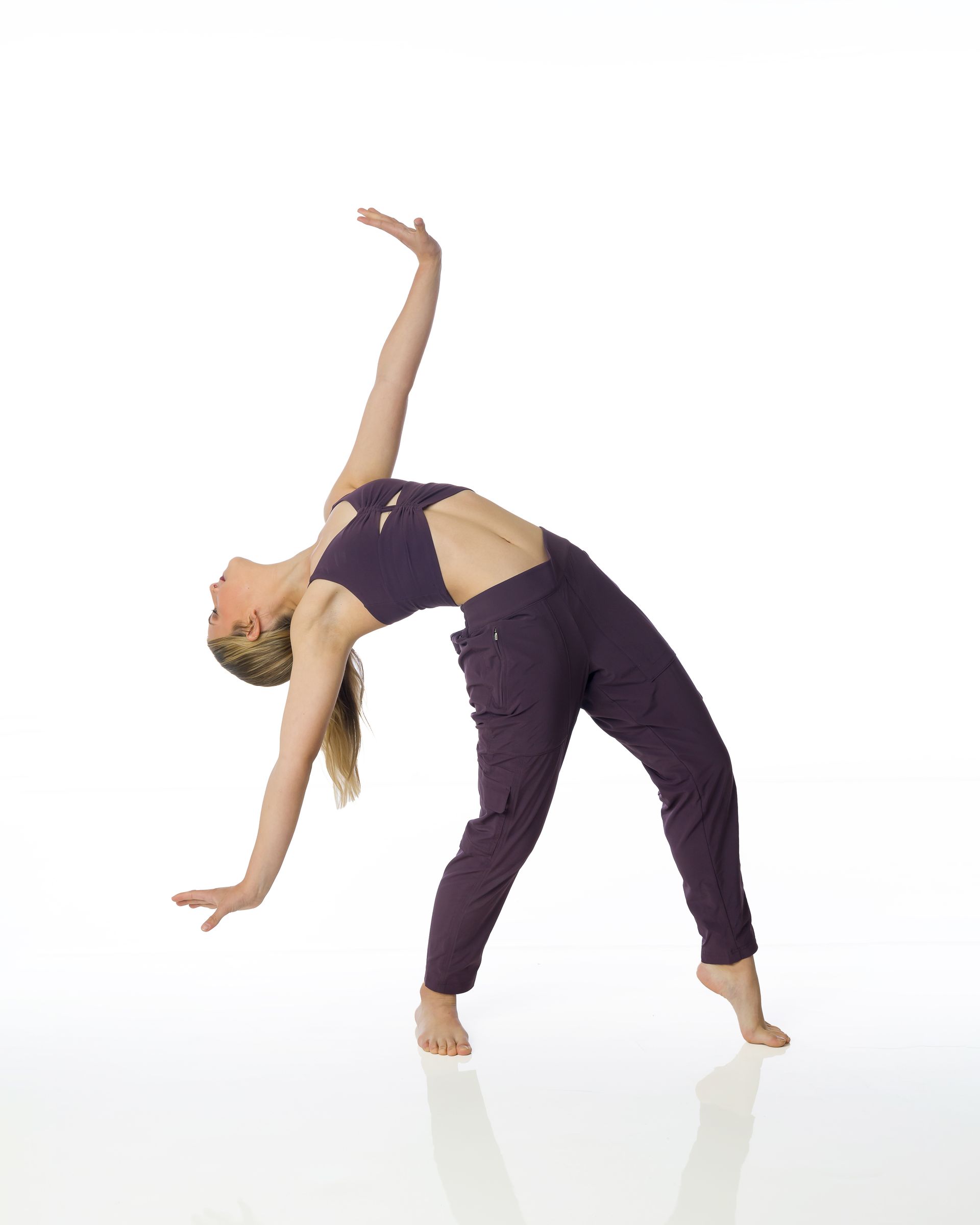 Woman in purple yoga clothes arching backward in a dance pose on a white background