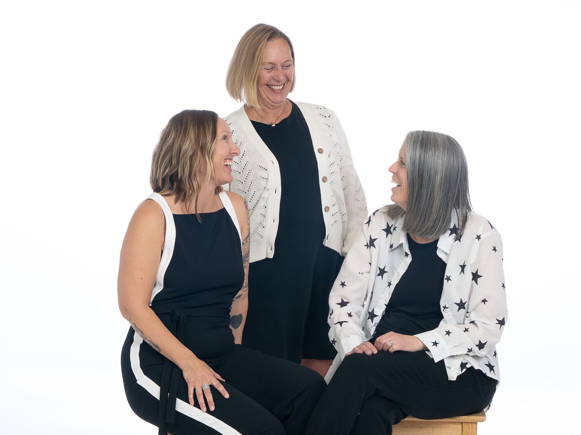 Three women seated and standing, smiling in a bright studio setting.