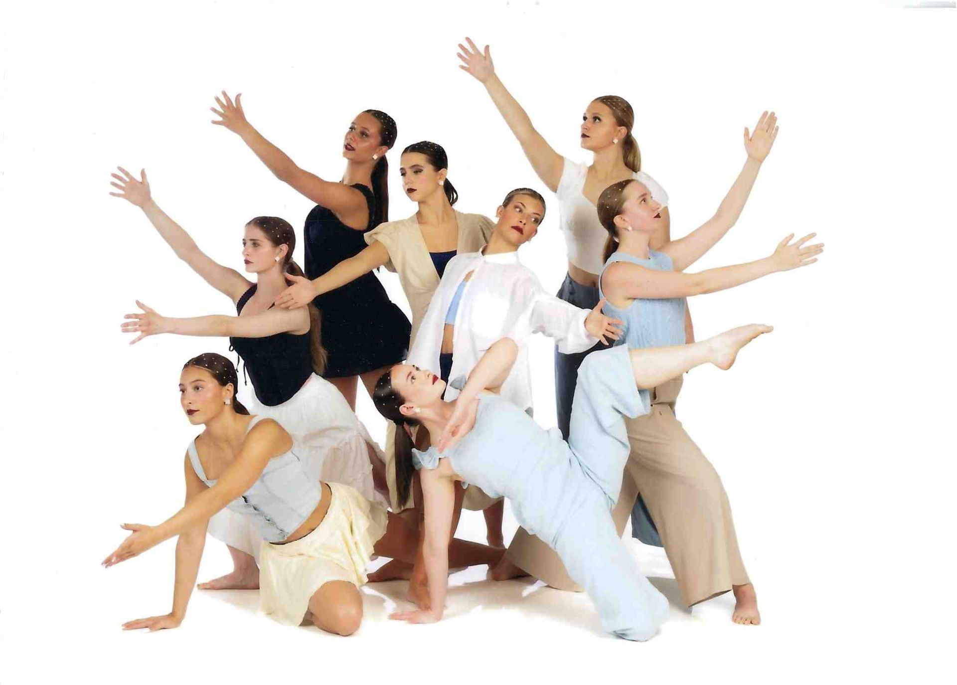 Group of dancers posing in white and black outfits with arms raised against a white background