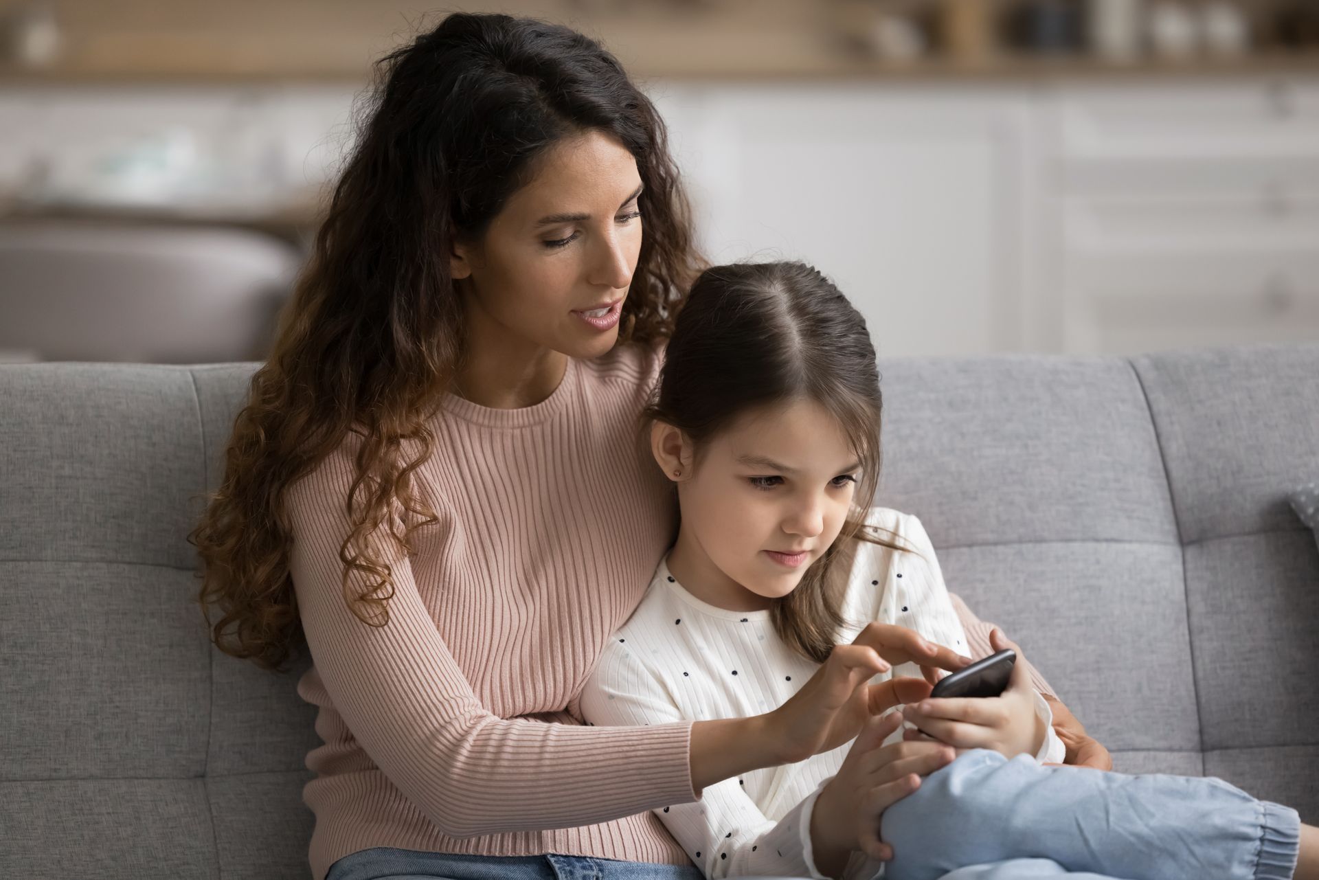 Woman and child sitting on a couch, looking at a smartphone together