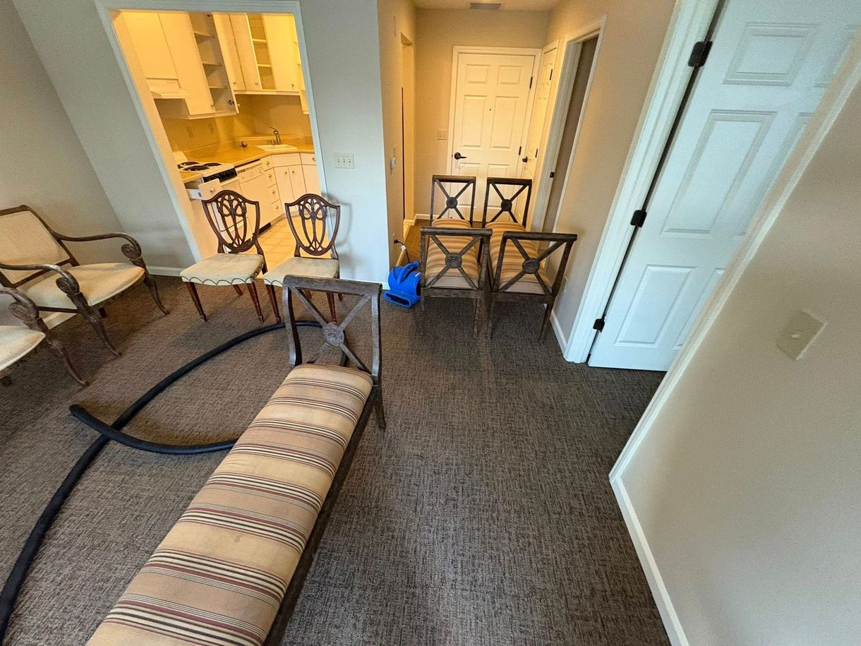 Carpeted room with a rolled rug, two folding chairs, and a hallway leading to a kitchen area