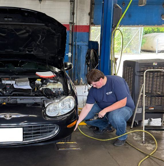 Mechanic inspecting a black car with hood open in a garage, holding an air hose | Libertyville Kar Care