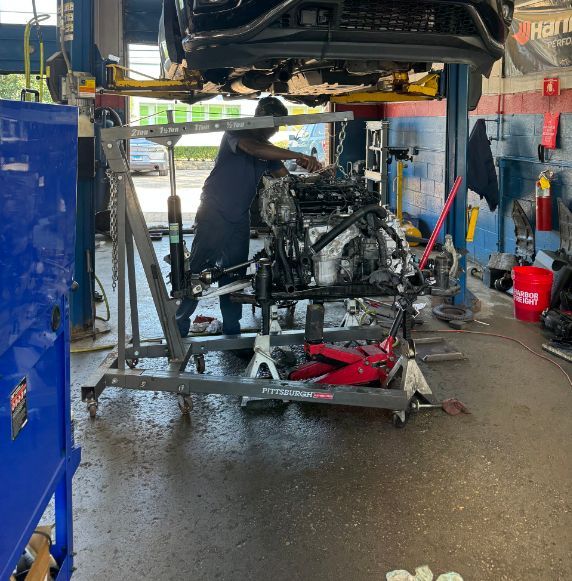 Mechanic working on car engine, supported by a hoist, in a garage | Libertyville Kar Care