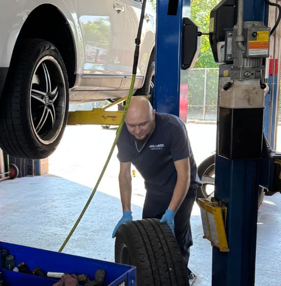 Mechanic replacing a tire on a white car lifted on a blue hydraulic lift; shop setting | Libertyville Kar Care