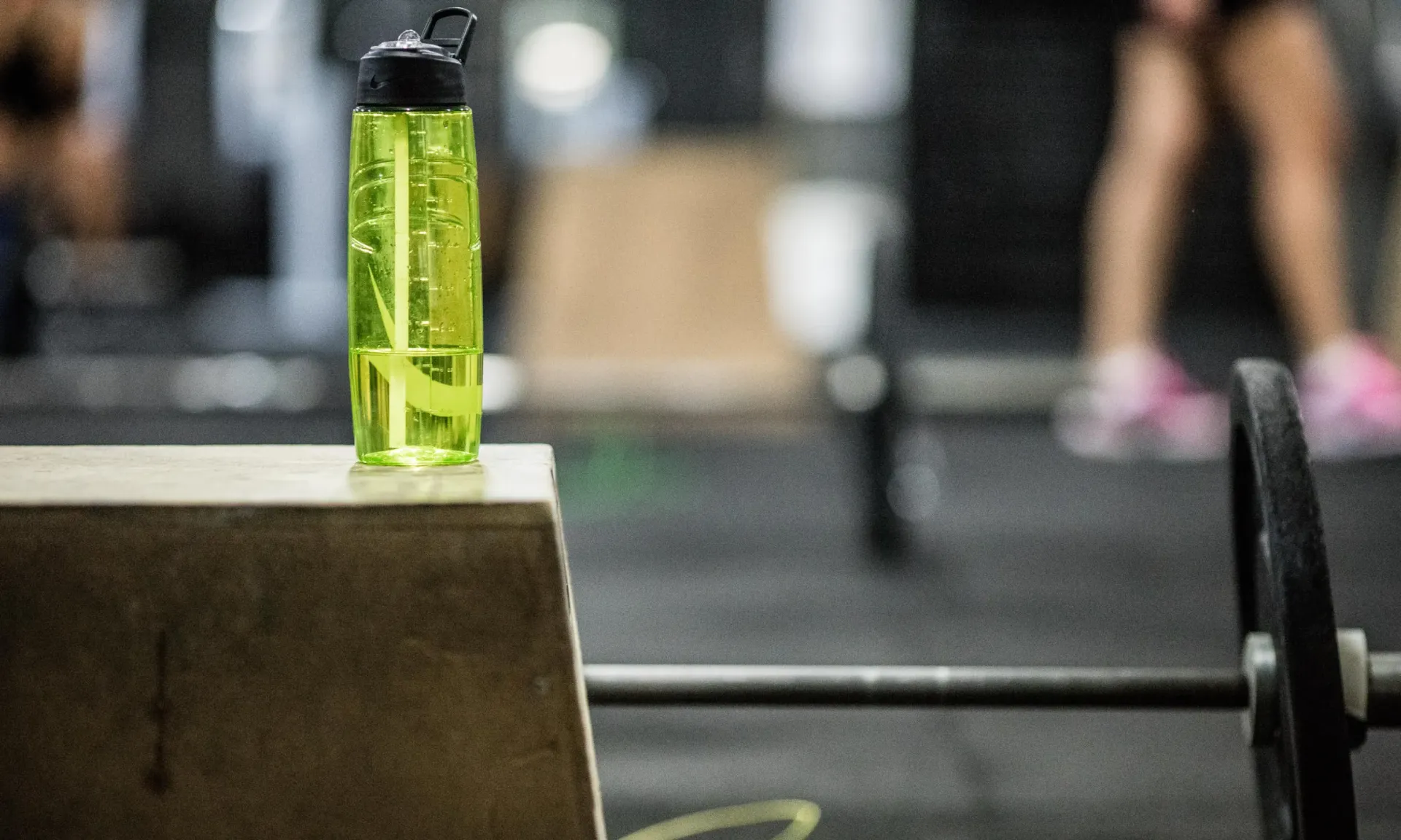 Green water bottle on a gym bench with blurred people in the background