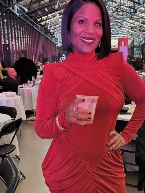 Woman in a red dress smiling and holding a drink at a banquet hall event.