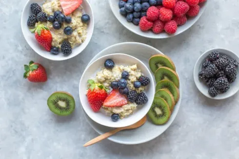 Bowls of yogurt topped with berries and kiwi slices on a light gray surface