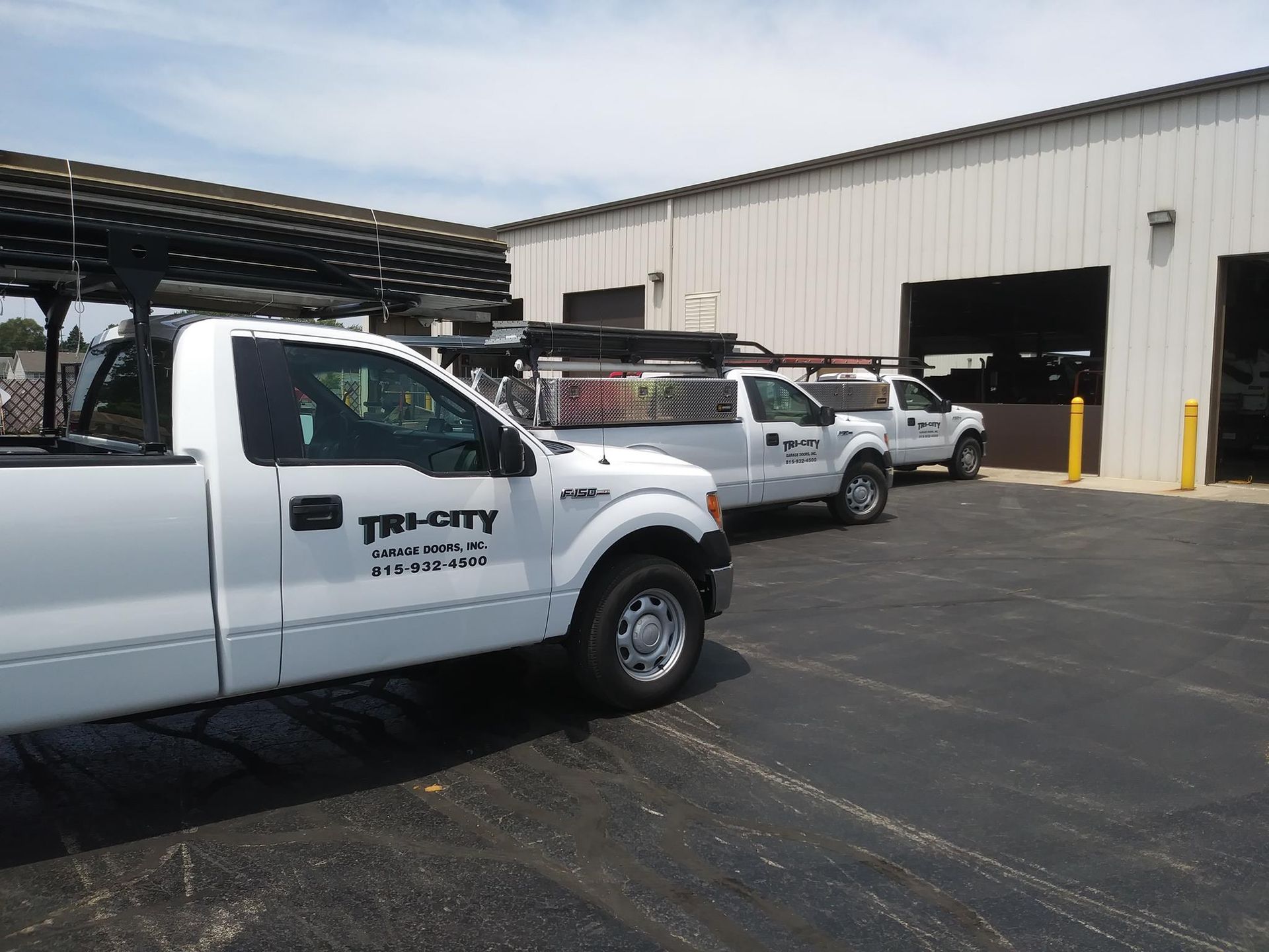 Three white service trucks parked outside an industrial warehouse garage.