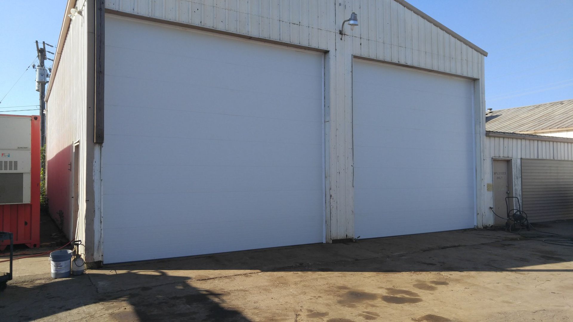 Two large white garage doors on a metal warehouse building in an industrial lot