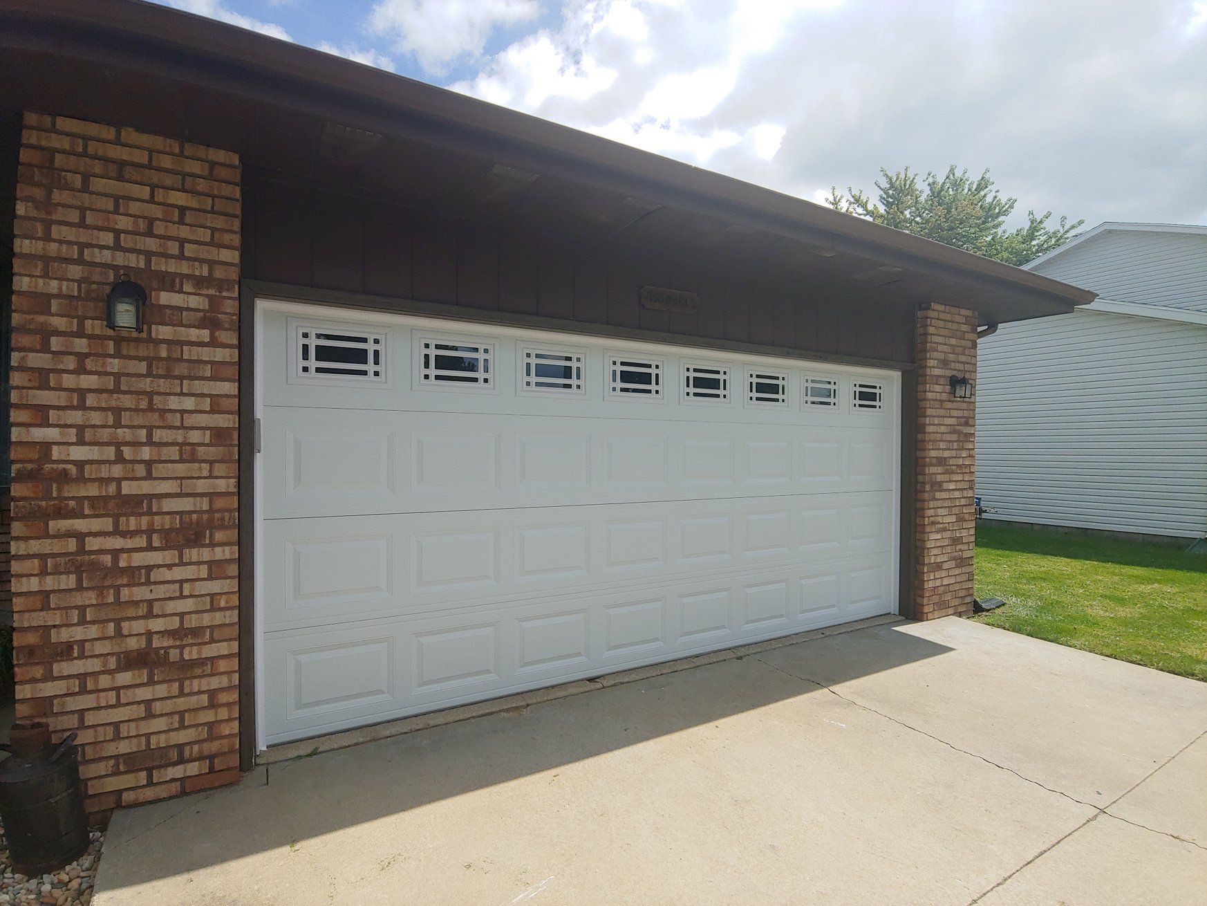 White garage door on a brick house with a concrete driveway and lawn beside it