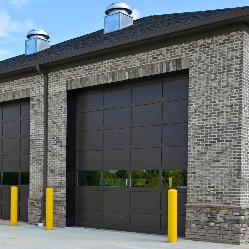 Modern brick building with a dark garage door and yellow safety bollards