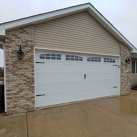White garage door on a house with beige siding and stone exterior, viewed from the driveway