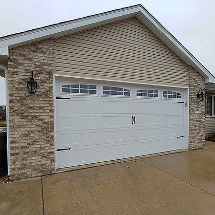 Single-car garage with white door, tan siding, and stone facade on a wet driveway