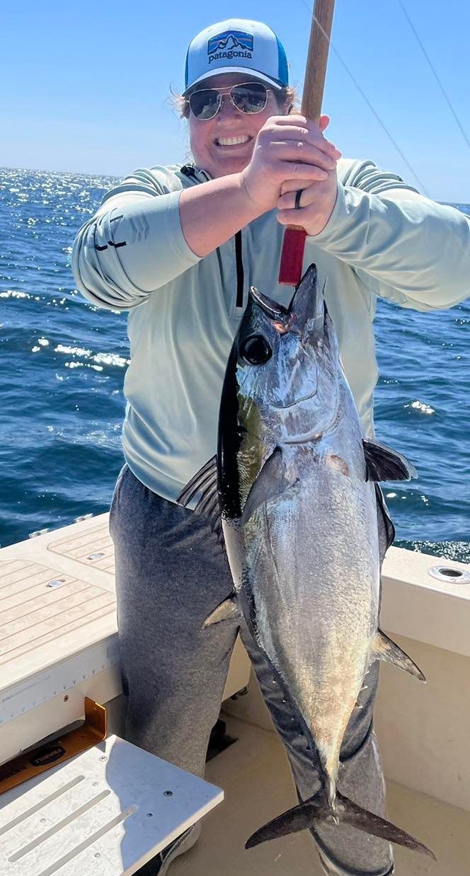 Person on a boat holding a large fish by the gills on a sunny day, ocean in the background