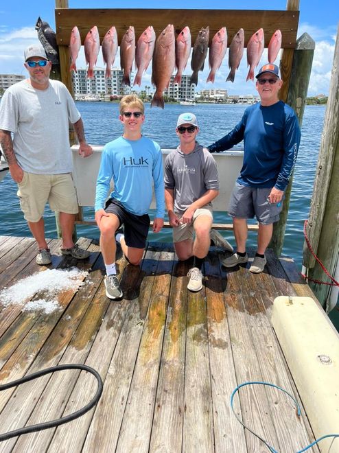 Four people posing on a fishing boat deck with a row of freshly caught fish hanging behind them.