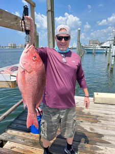 Man holding a large red fish on a dock beside the marina under a blue sky