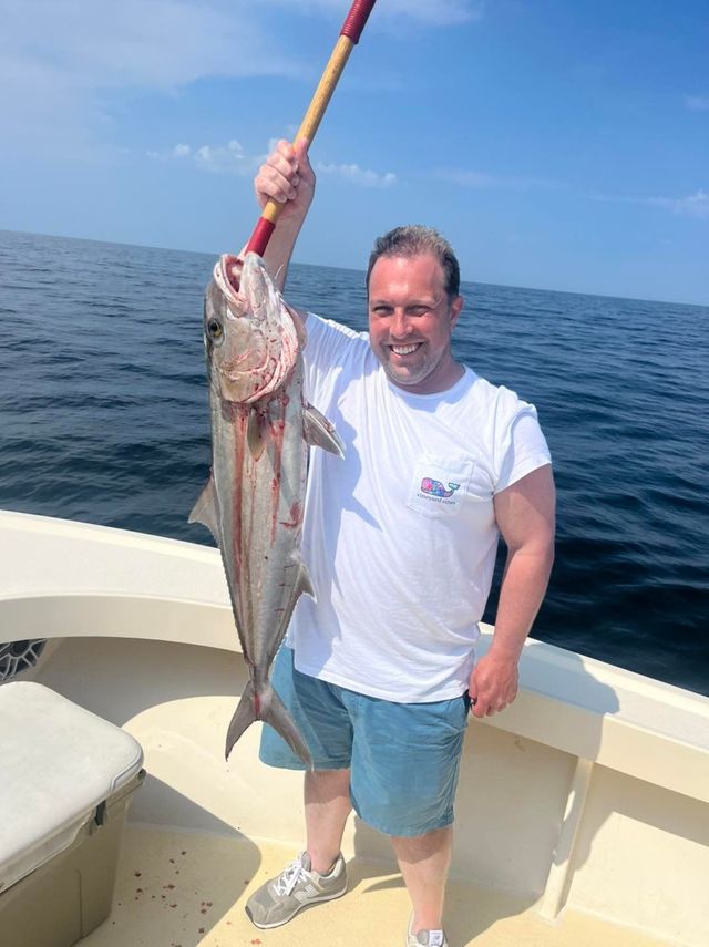 Man on a boat holding up a large fish over the ocean