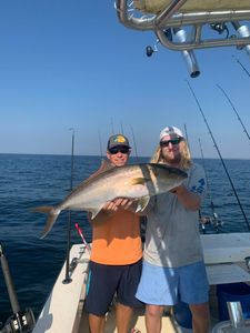 Two anglers on a boat holding a large fish, with open ocean and clear blue sky behind them.