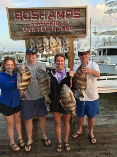 Four people posing with large fish outside Boshamp's Seafood Oyster House at a marina
