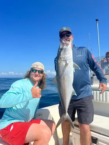 Two people on a boat holding a large silver fish under a clear blue sky.