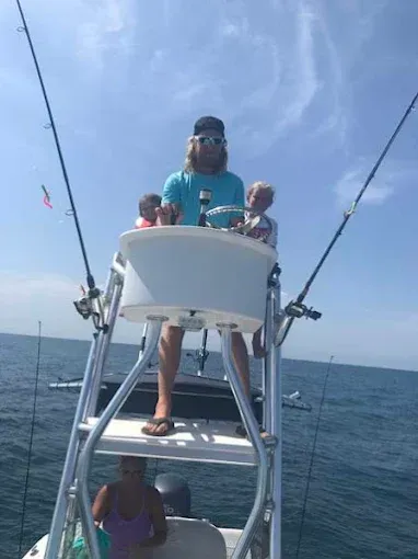 Person standing on a boat’s flybridge over open water, holding onto the helm with fishing rods visible.