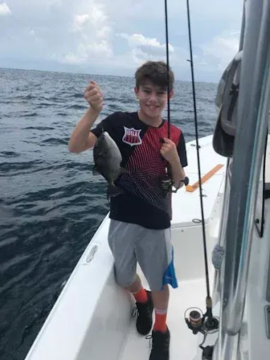 Person holding a fish on a boat at sea, with fishing rods and calm water in the background.