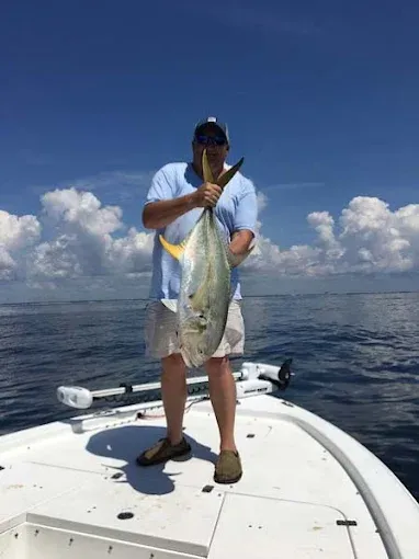 Person on a boat holding a large fish over the ocean under a blue sky